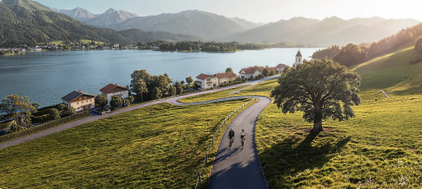Two cyclists on a paved path beside a mountain lake